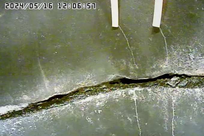 Dark wall with a large horizontal crack filled with dark material; two white strips hang above.