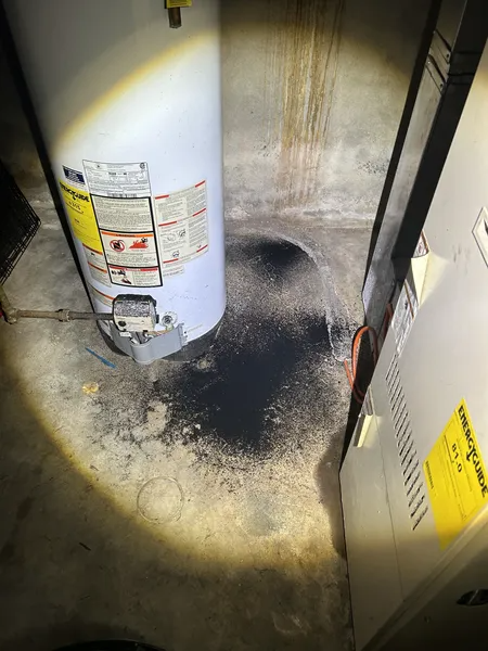 Water heater and furnace in a basement. Dark spill on floor.