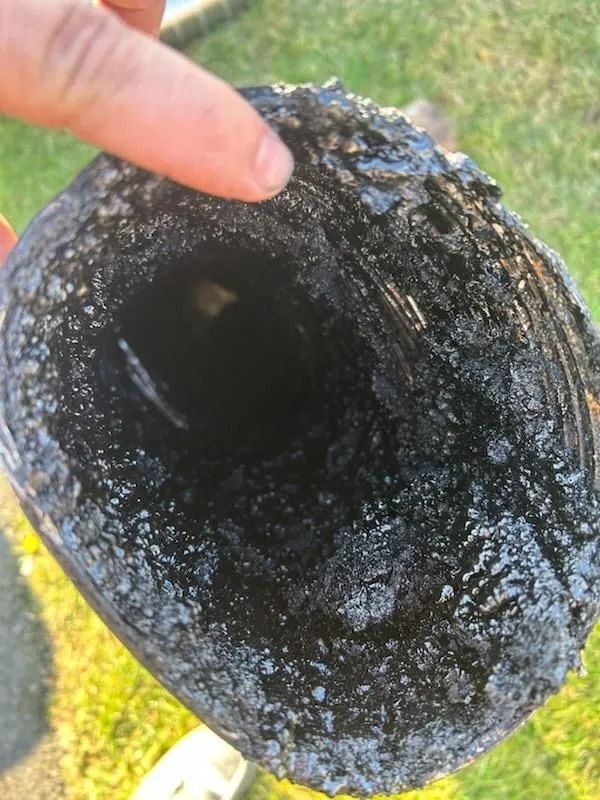 A section of a black, cylindrical pipe interior, heavily coated with soot.
