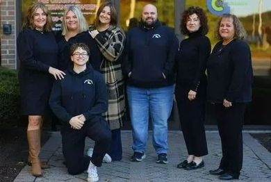 Group of seven people posing outside a building; most in black attire.