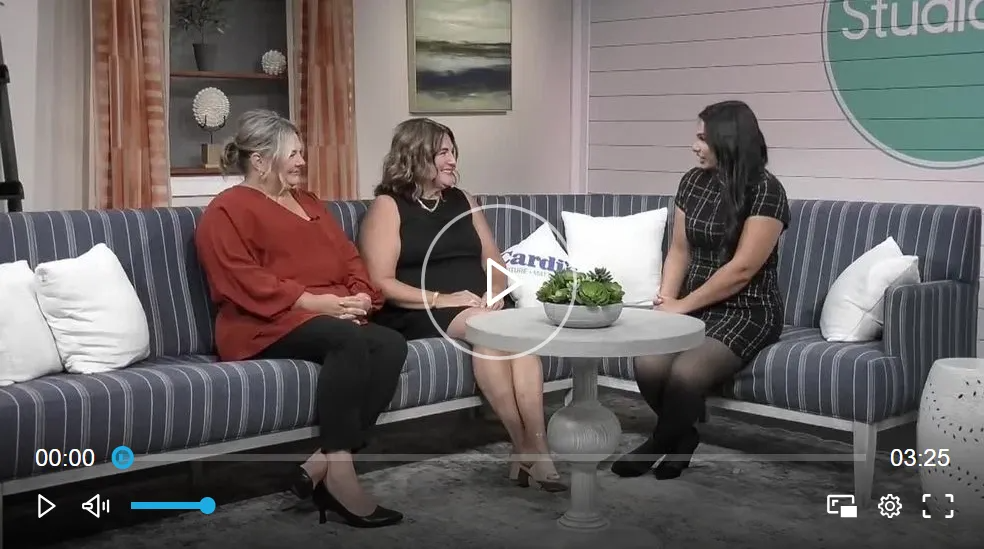 Three people seated on a striped sofa in a studio setting, engaged in conversation.