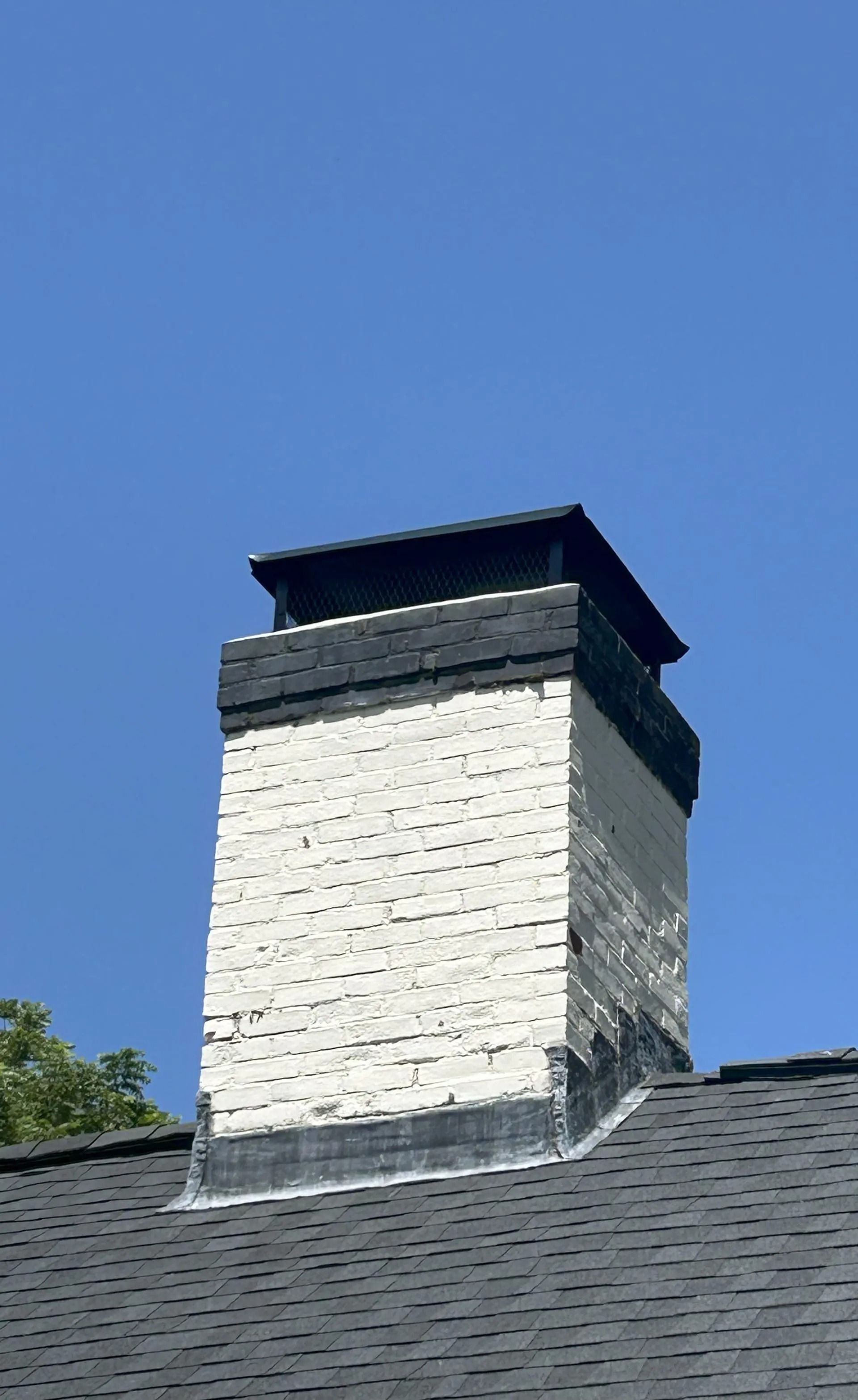 Brick chimney with black cap against a blue sky, on a dark roof.