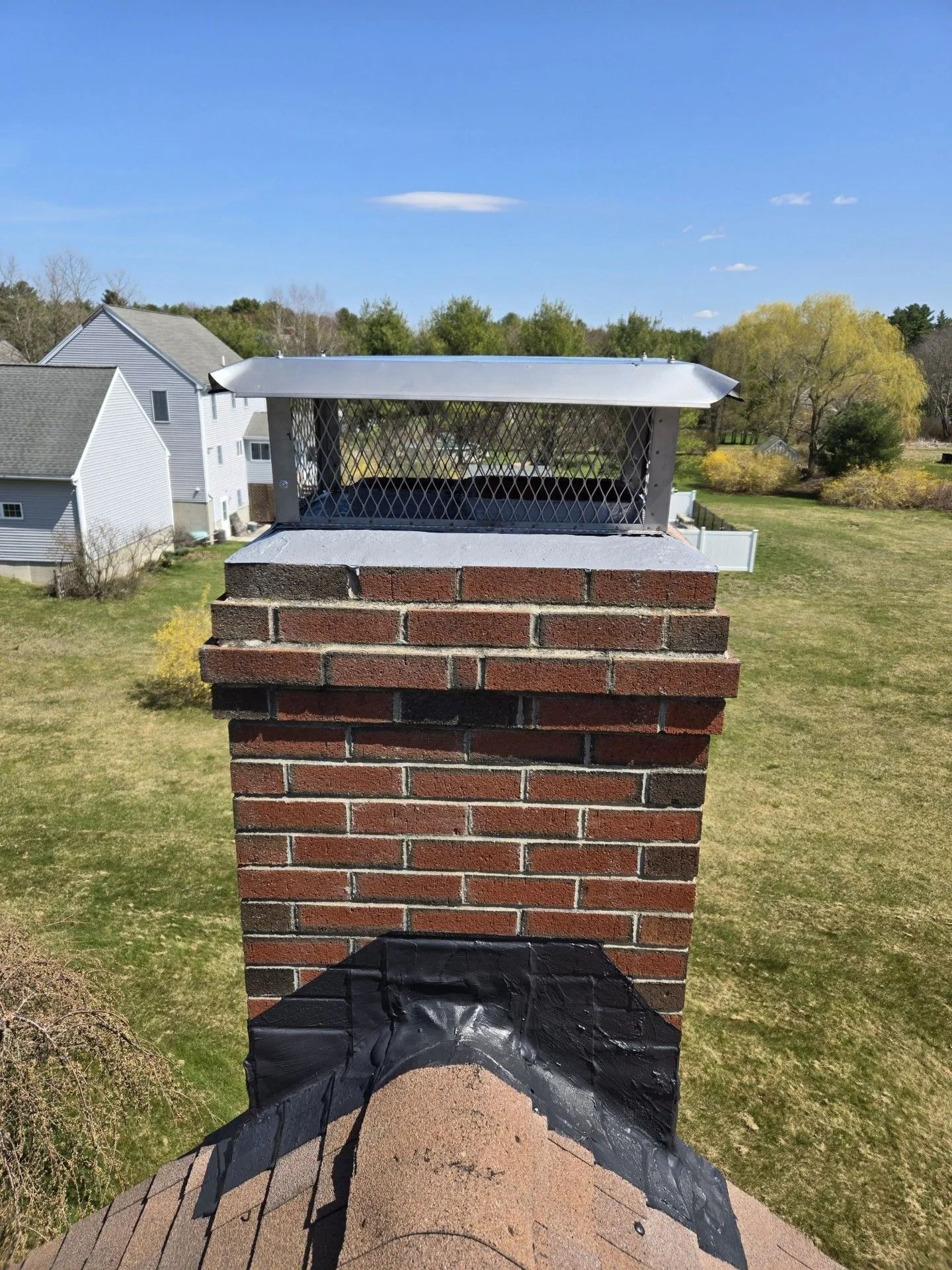 Brick chimney with metal cap on rooftop, blue sky background.