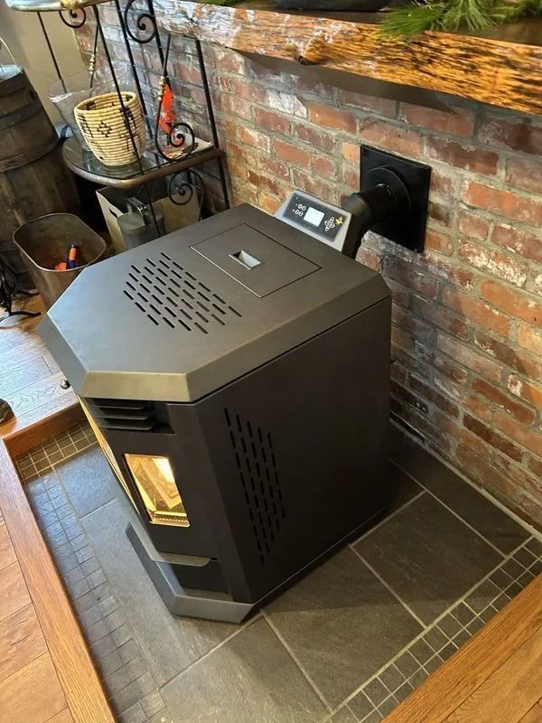 Black pellet stove against a brick wall, venting outside. The stove is on tiled floor.