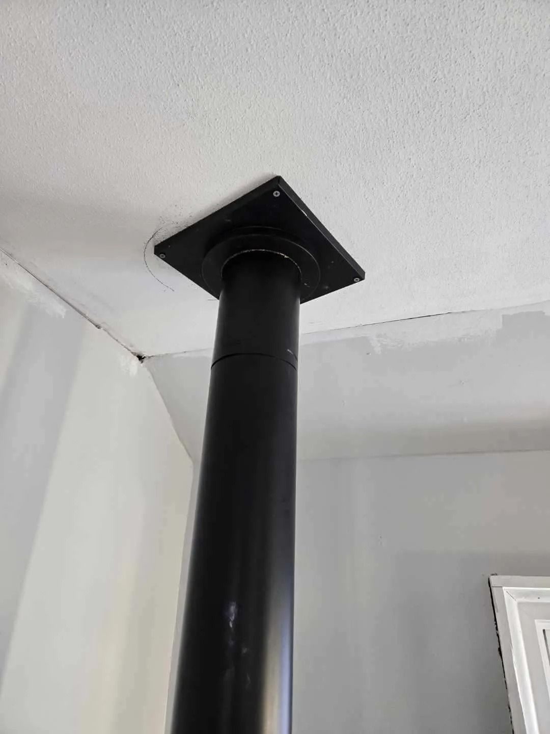 Black stove pipe extending from ceiling, mounted with a square plate.