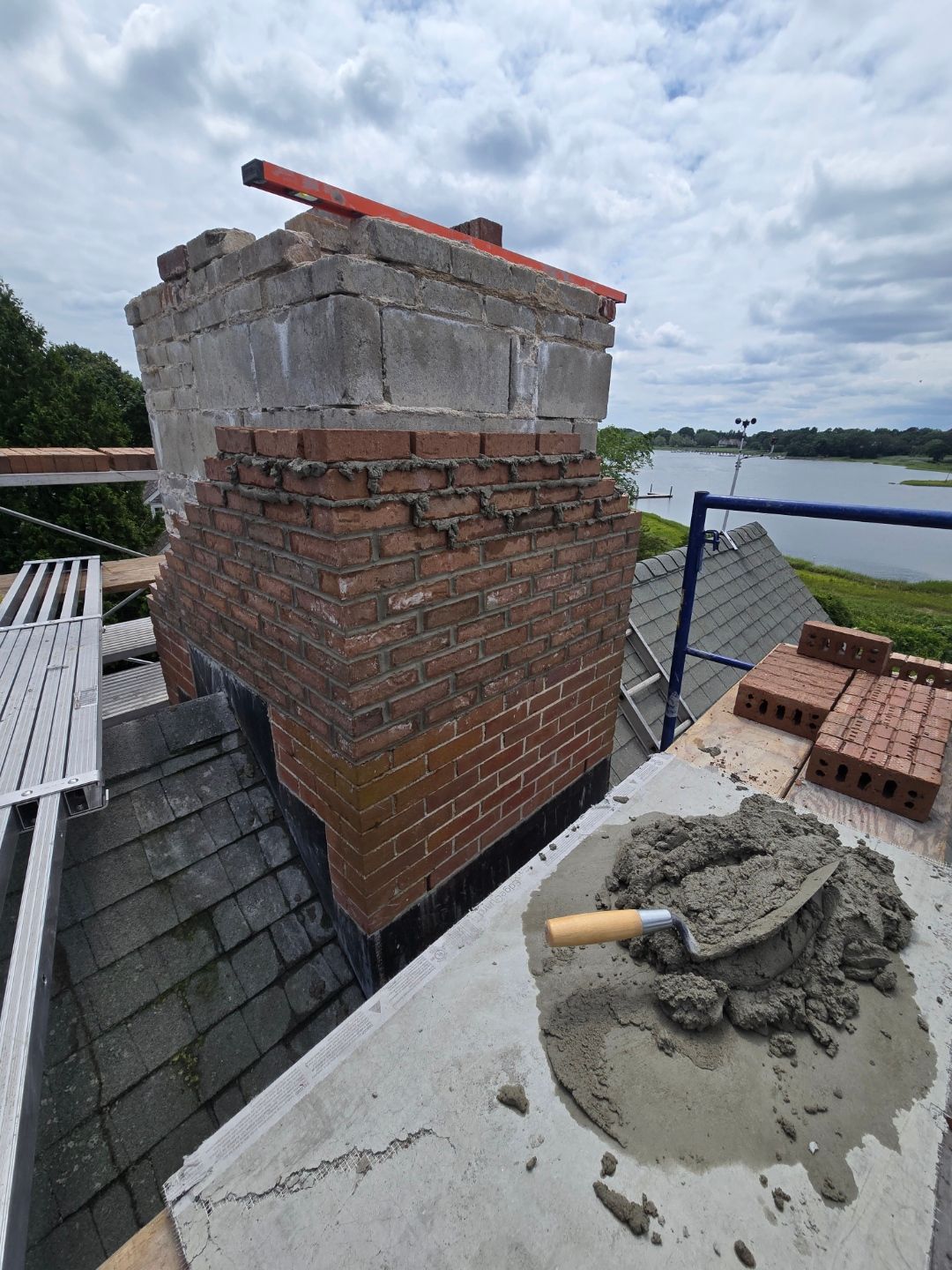 Chimney repair with mortar and bricks on roof, lake background.