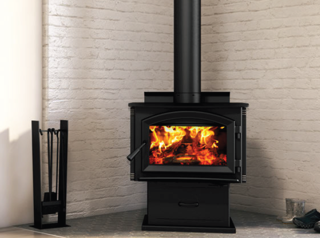 Black wood stove with a roaring fire in a brick-lined room, with fireplace tools on the left.