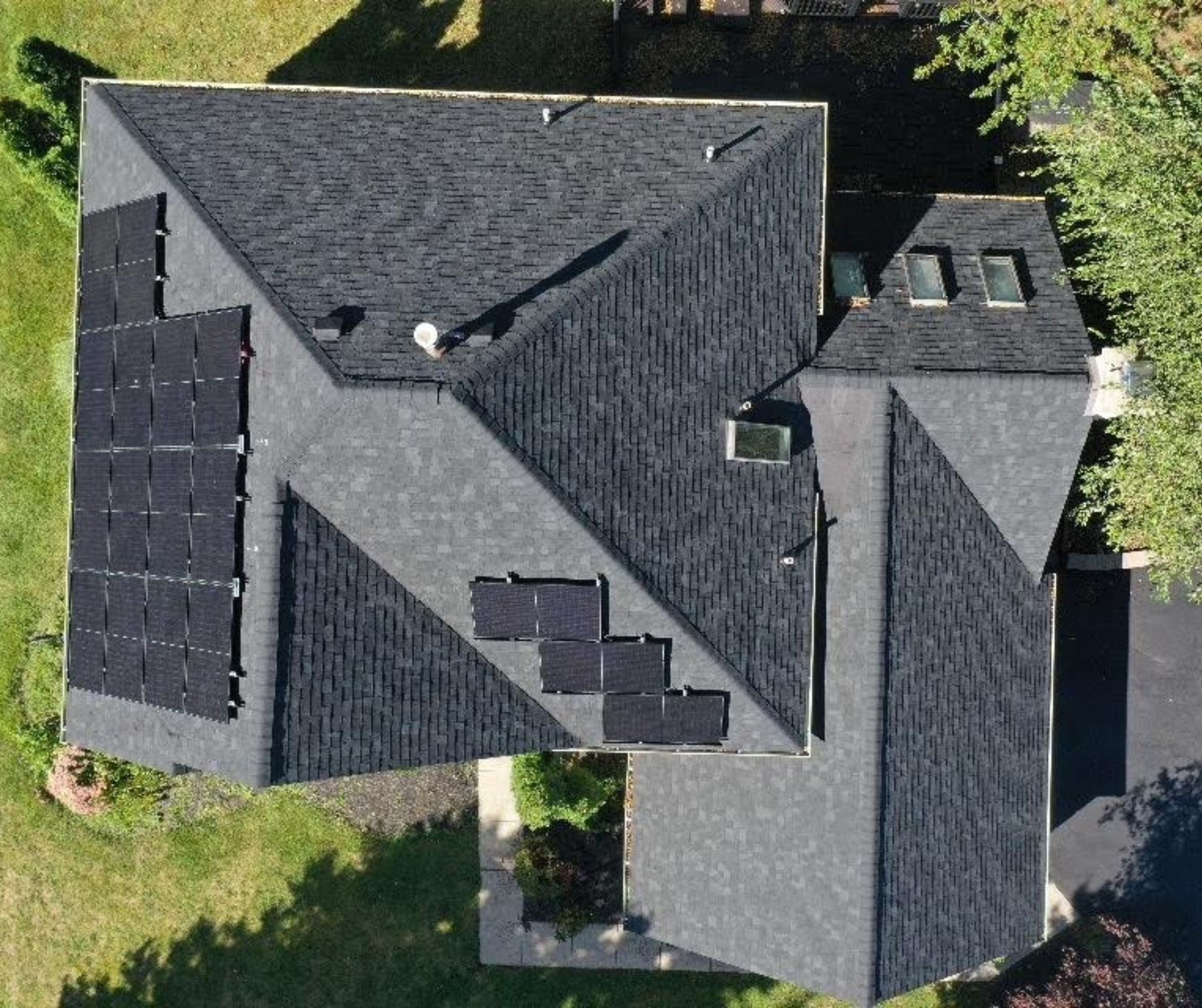 Overhead view of a house with solar panels on a dark shingled roof, set against a green lawn.