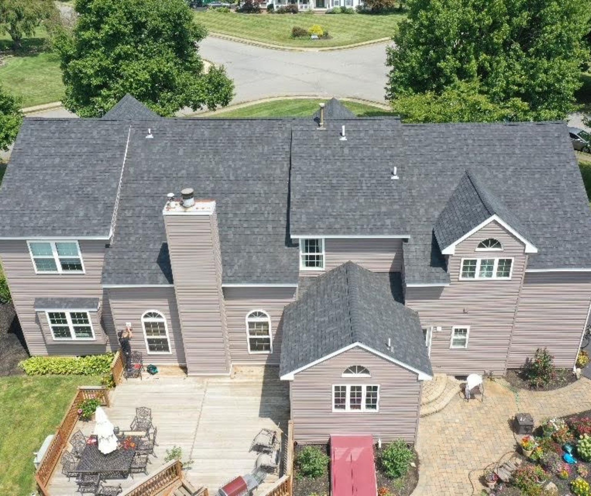 Aerial view of a gray-roofed house with a deck and landscaping.