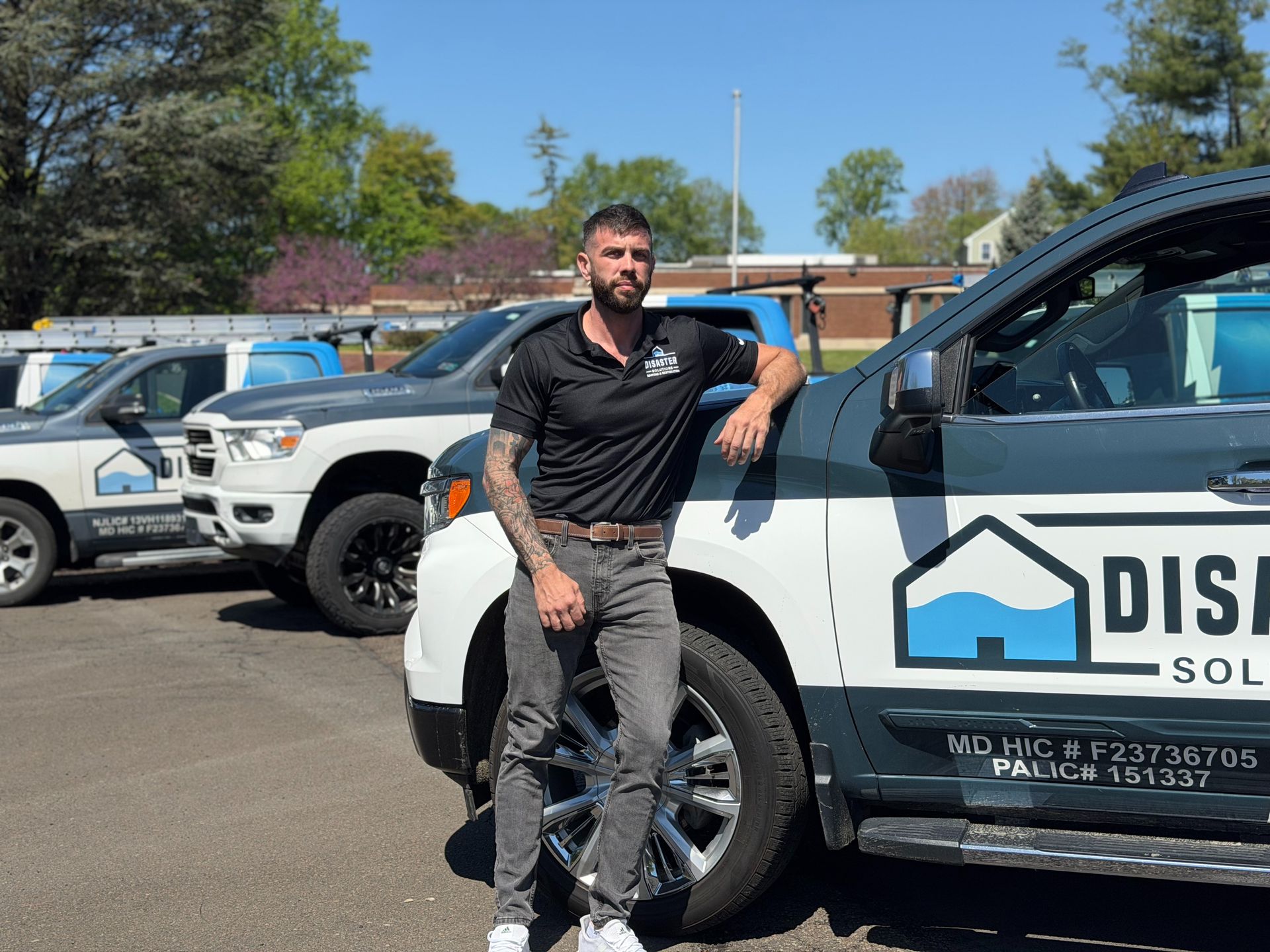 Man leaning on a white service truck in a parking lot under a clear blue sky