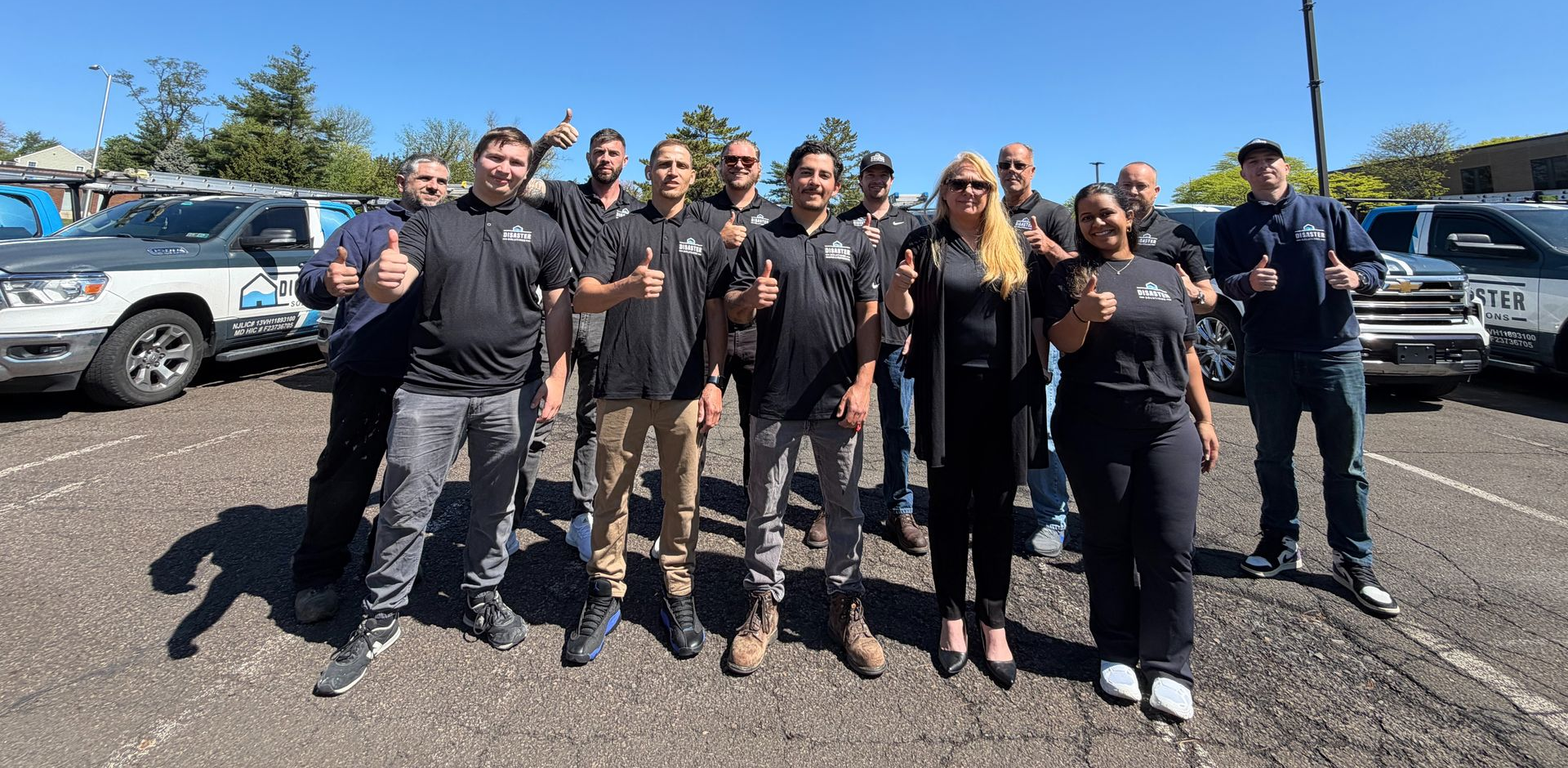 Group of people in black uniforms posing outdoors in a parking lot on a sunny day.