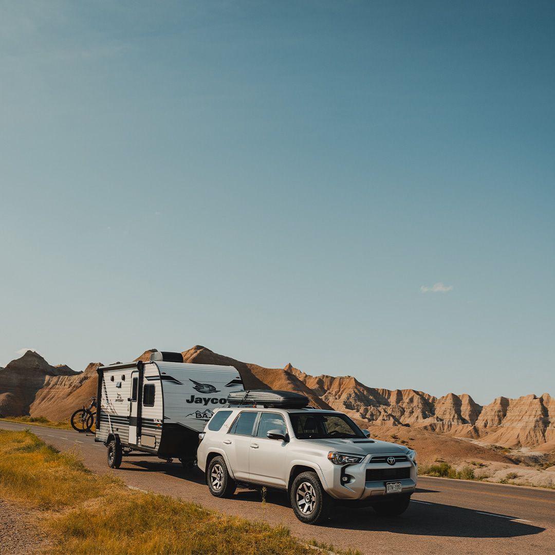 White RV parked on grassy shore with awning extended beside a calm blue lake under a cloudy sky