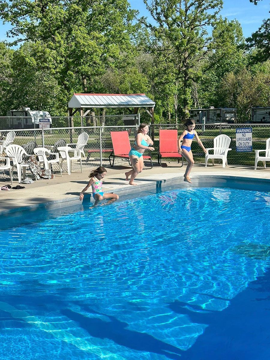 Three people in swimsuits about to jump into a blue swimming pool