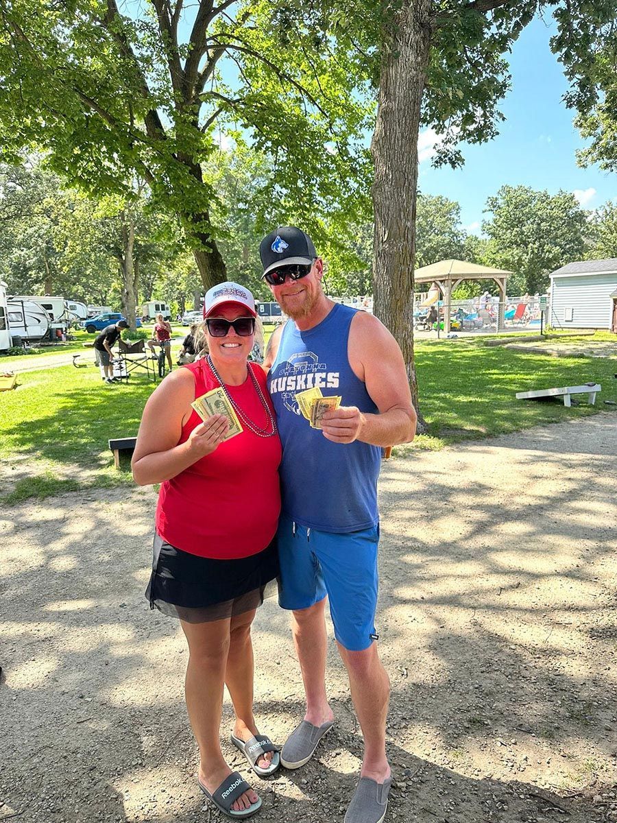 Two people hold money, standing outdoors at a park