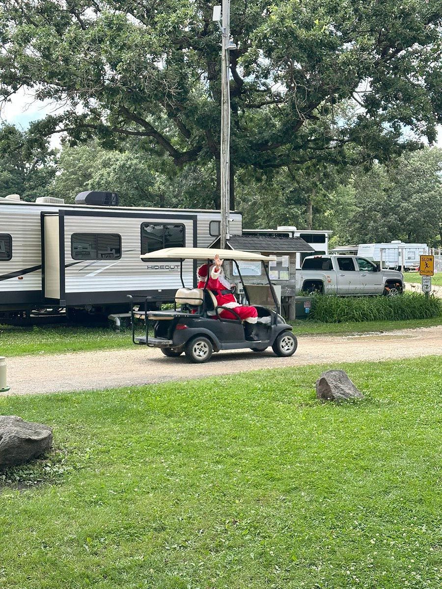 Person in Santa suit drives golf cart in a campground