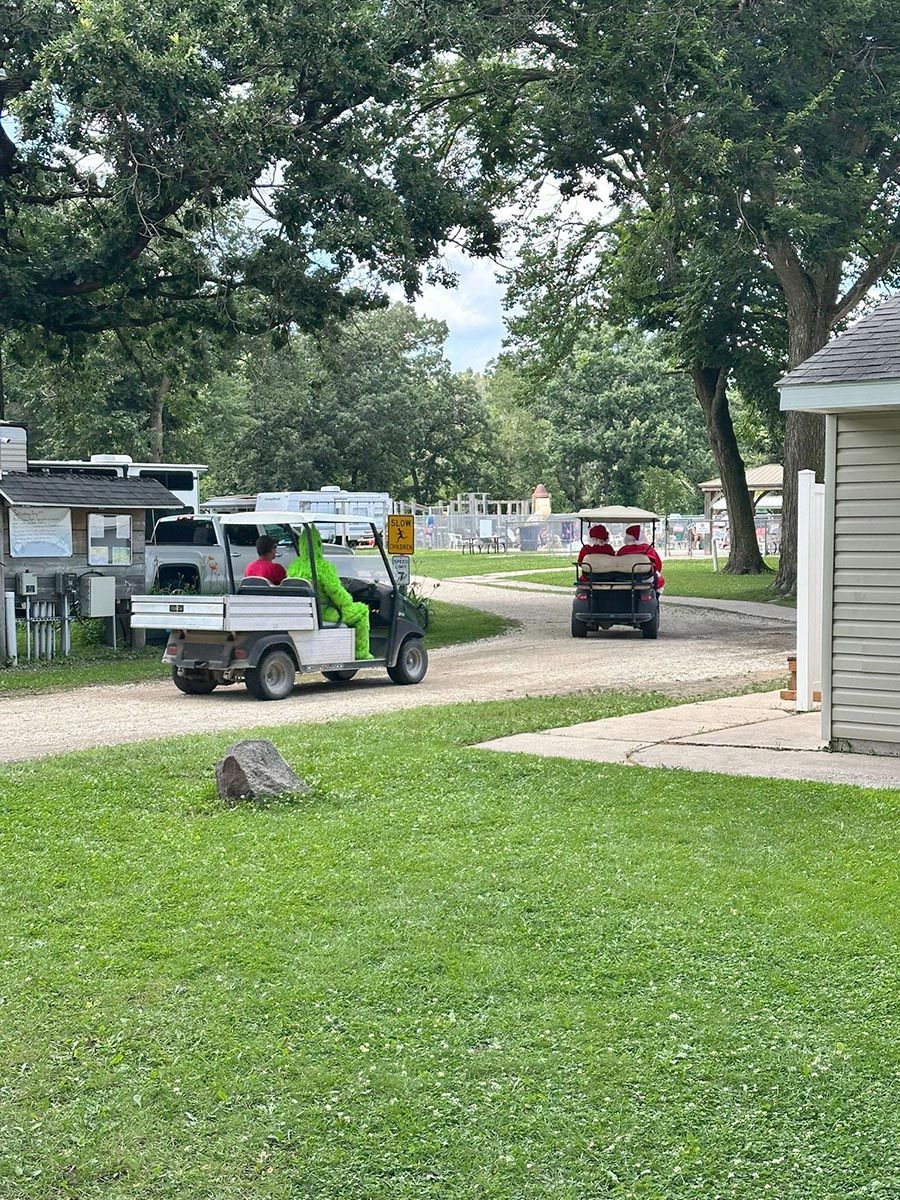Two golf carts driving on a gravel road, one with a green figure, one with a red figure