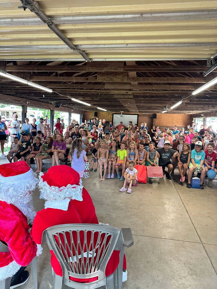 Two Santas facing a large crowd of people under a covered outdoor structure