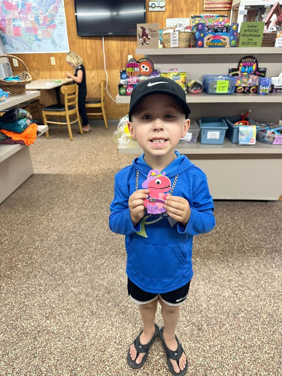 Young child smiles, holding a colorful craft