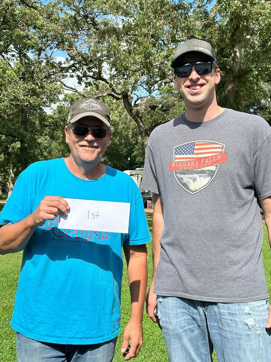 Two men in hats outdoors; one holds a white paper