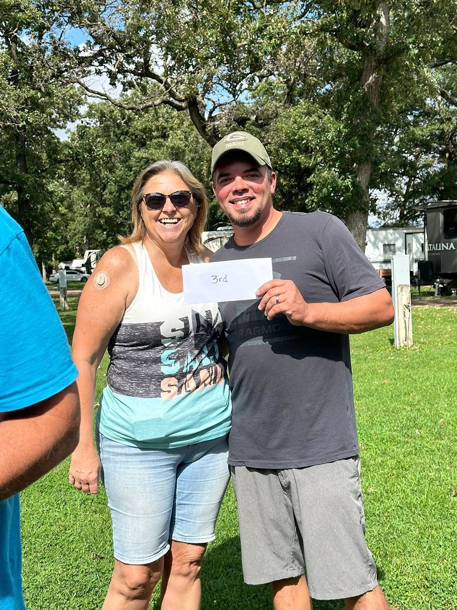 Man and woman smiling, holding a paper outdoors in a park