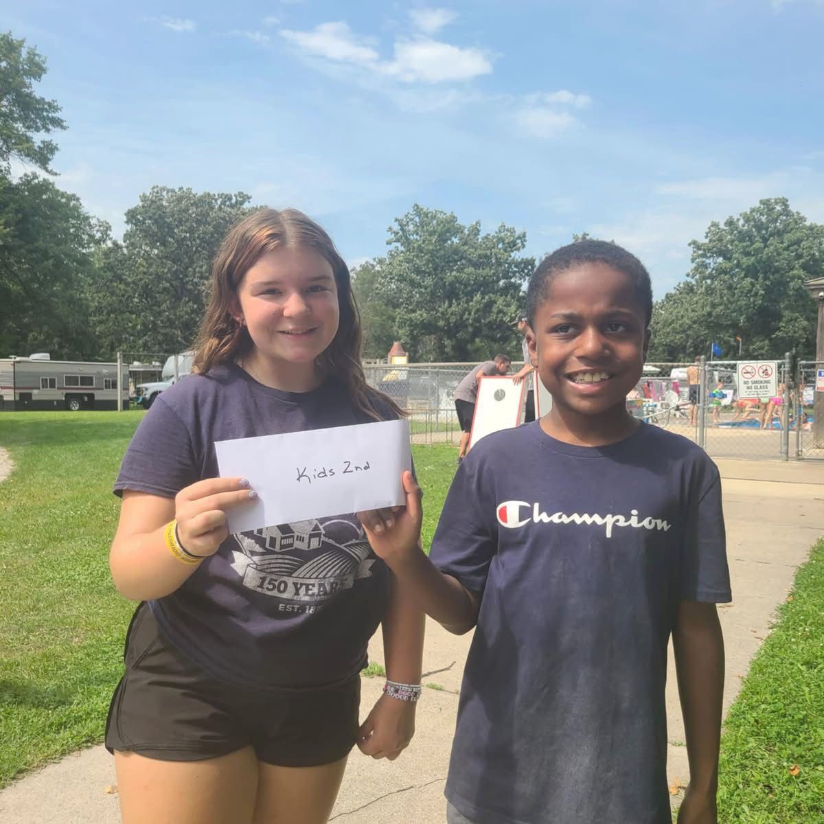 Two smiling teens holding a card outside