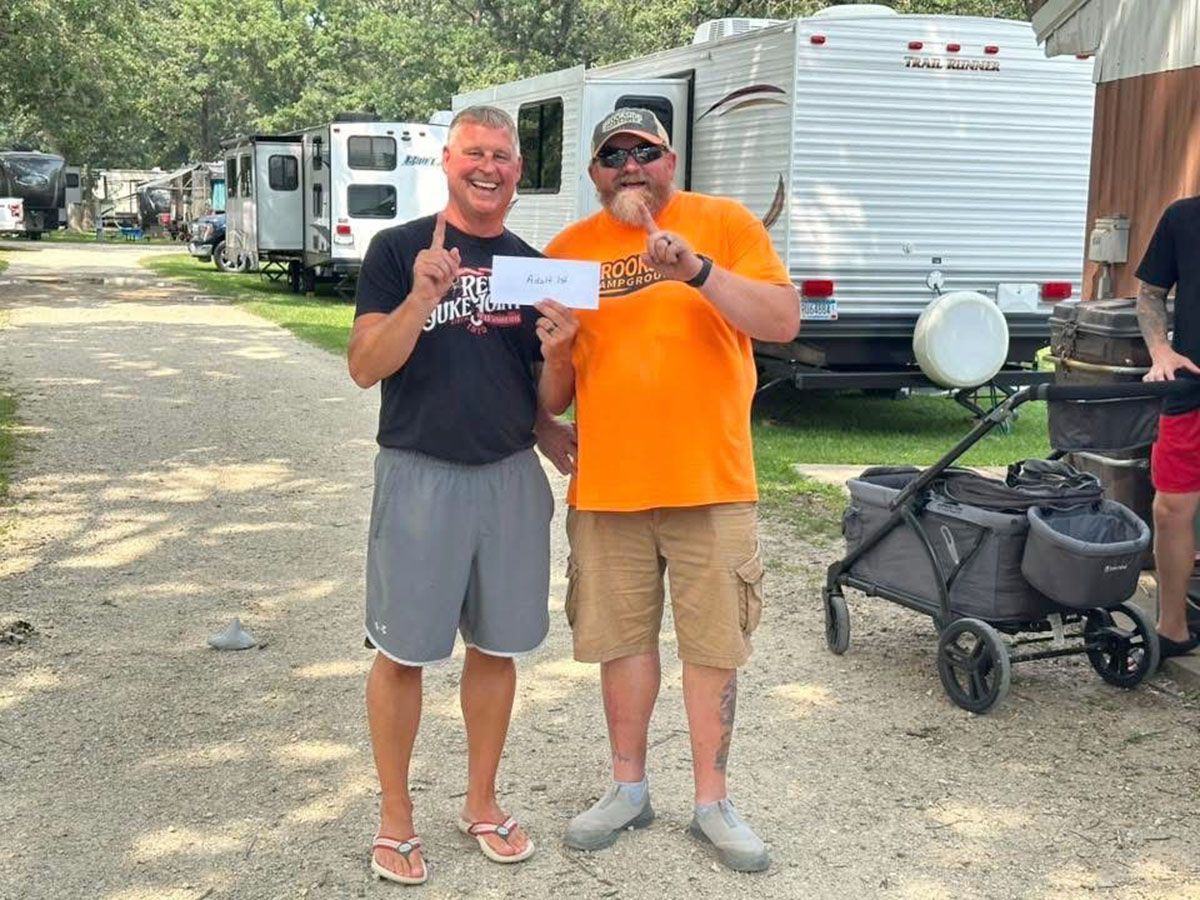 Two men holding a paper, outdoors near RVs