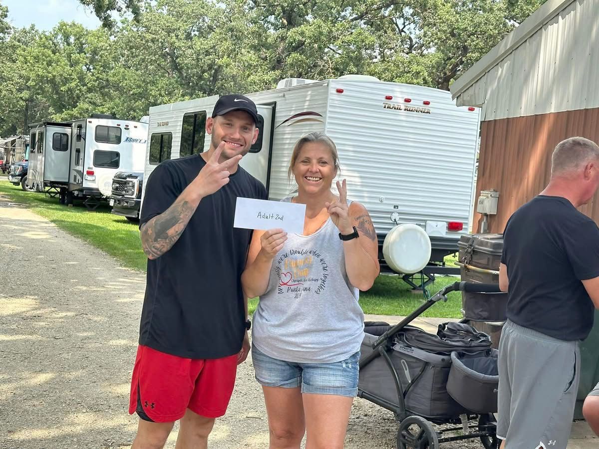 Two people holding a paper, smiling, in front of an RV park
