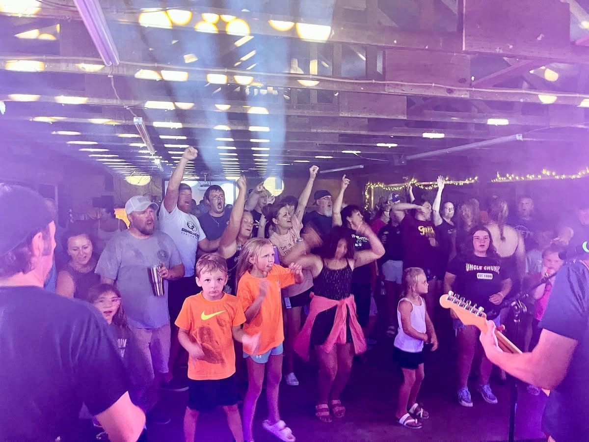 People dancing and enjoying a band performance under purple and white lights in a large space