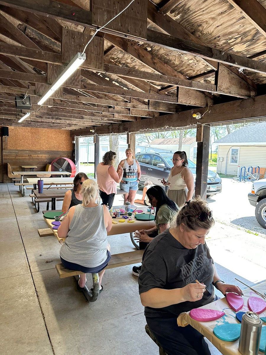 Group of people crafting at wooden tables under a covered outdoor structure