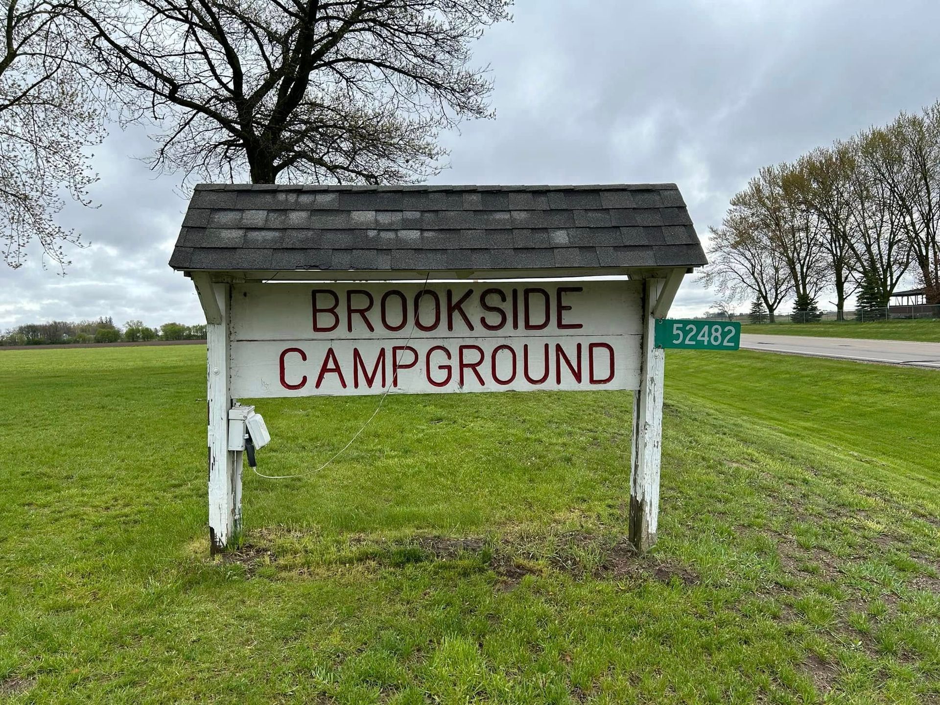 A sign for Brookside Campground is sitting in the middle of a grassy field.