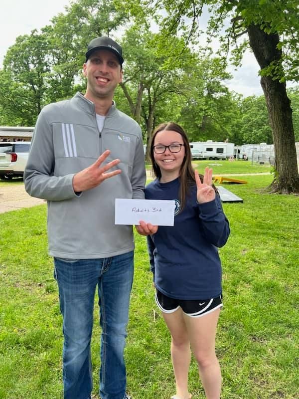 A man and a woman are standing next to each other in a park holding an envelope.