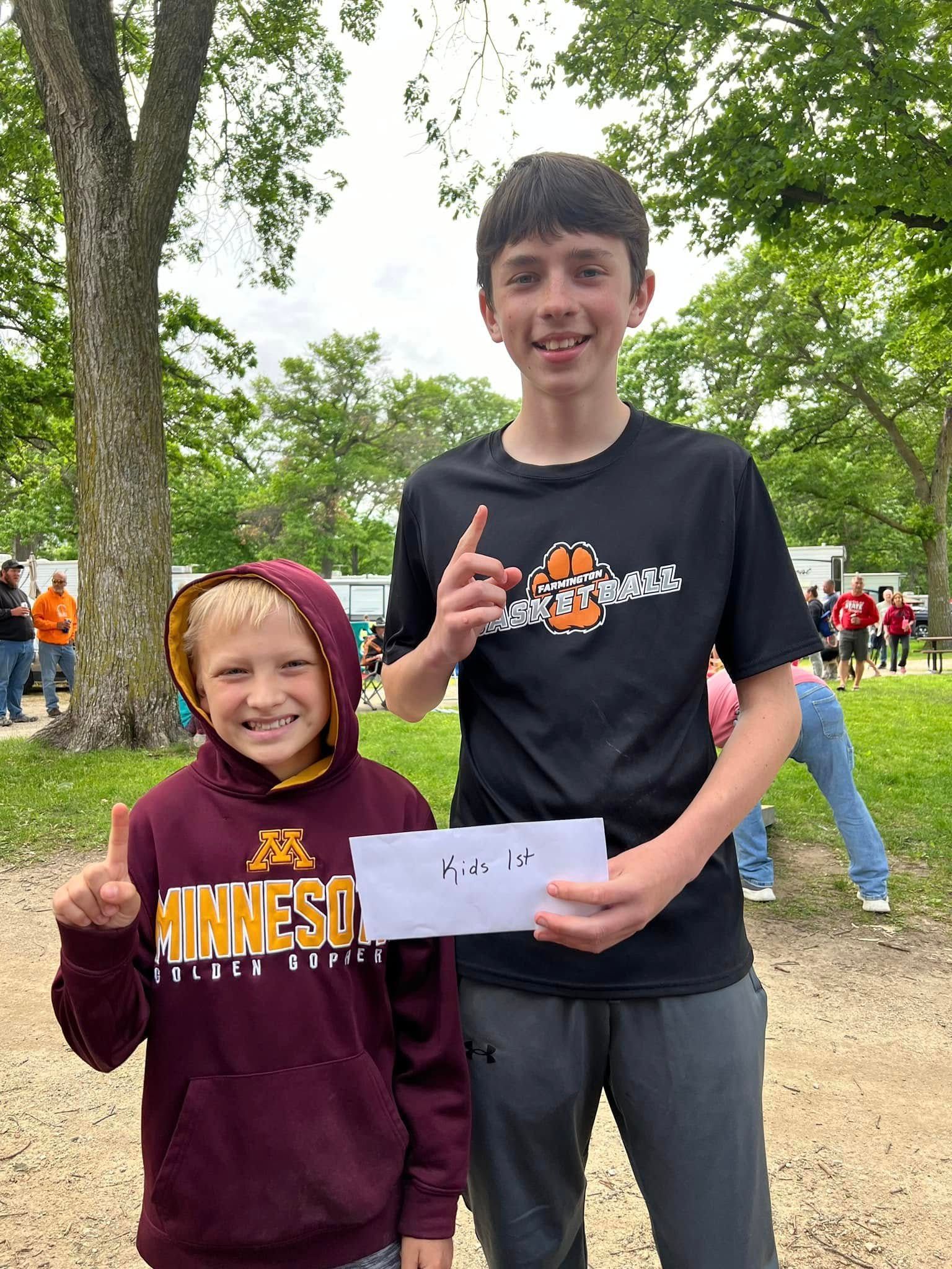 Two young boys are standing next to each other in a park holding an envelope.