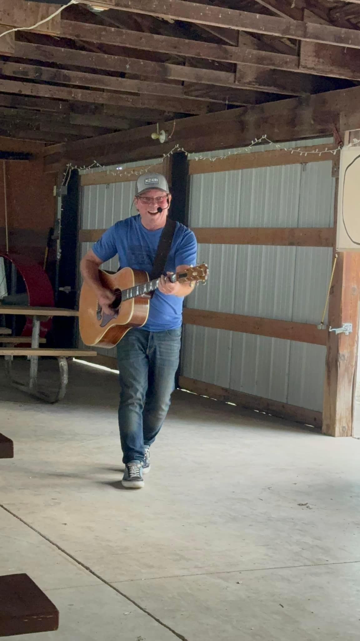A man is playing an acoustic guitar in a barn.