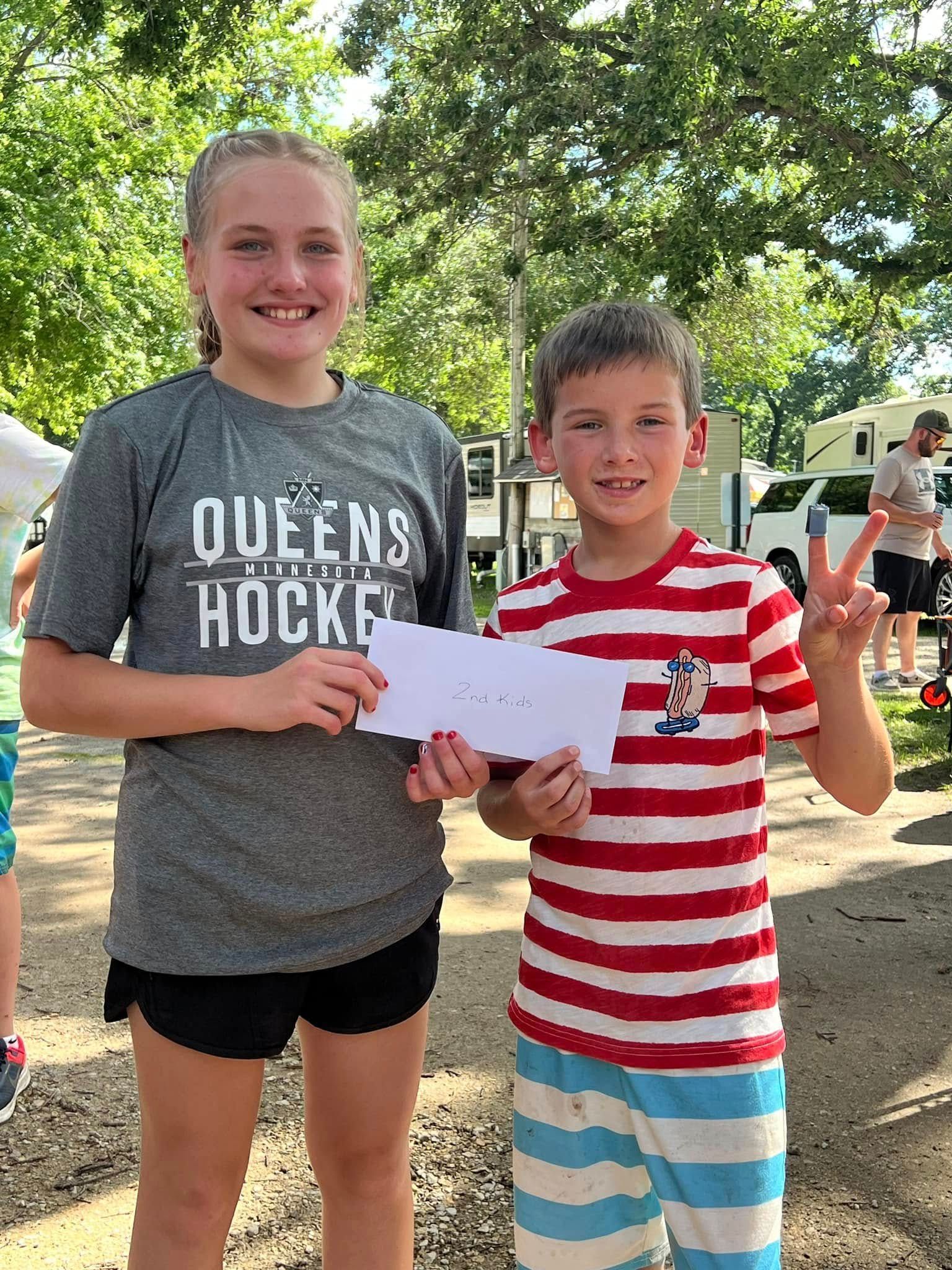 A boy and a girl are standing next to each other holding a check.