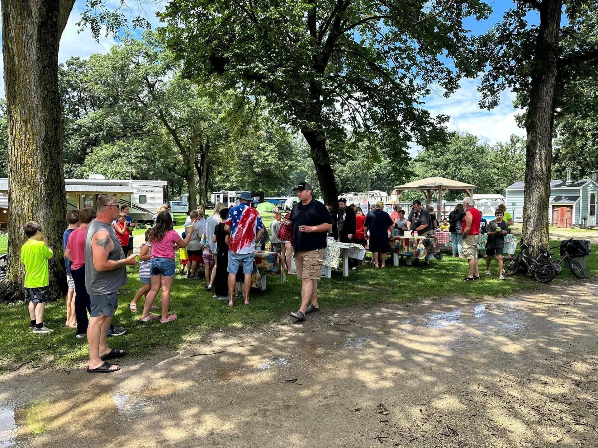 A group of people are standing around a picnic table in a park.