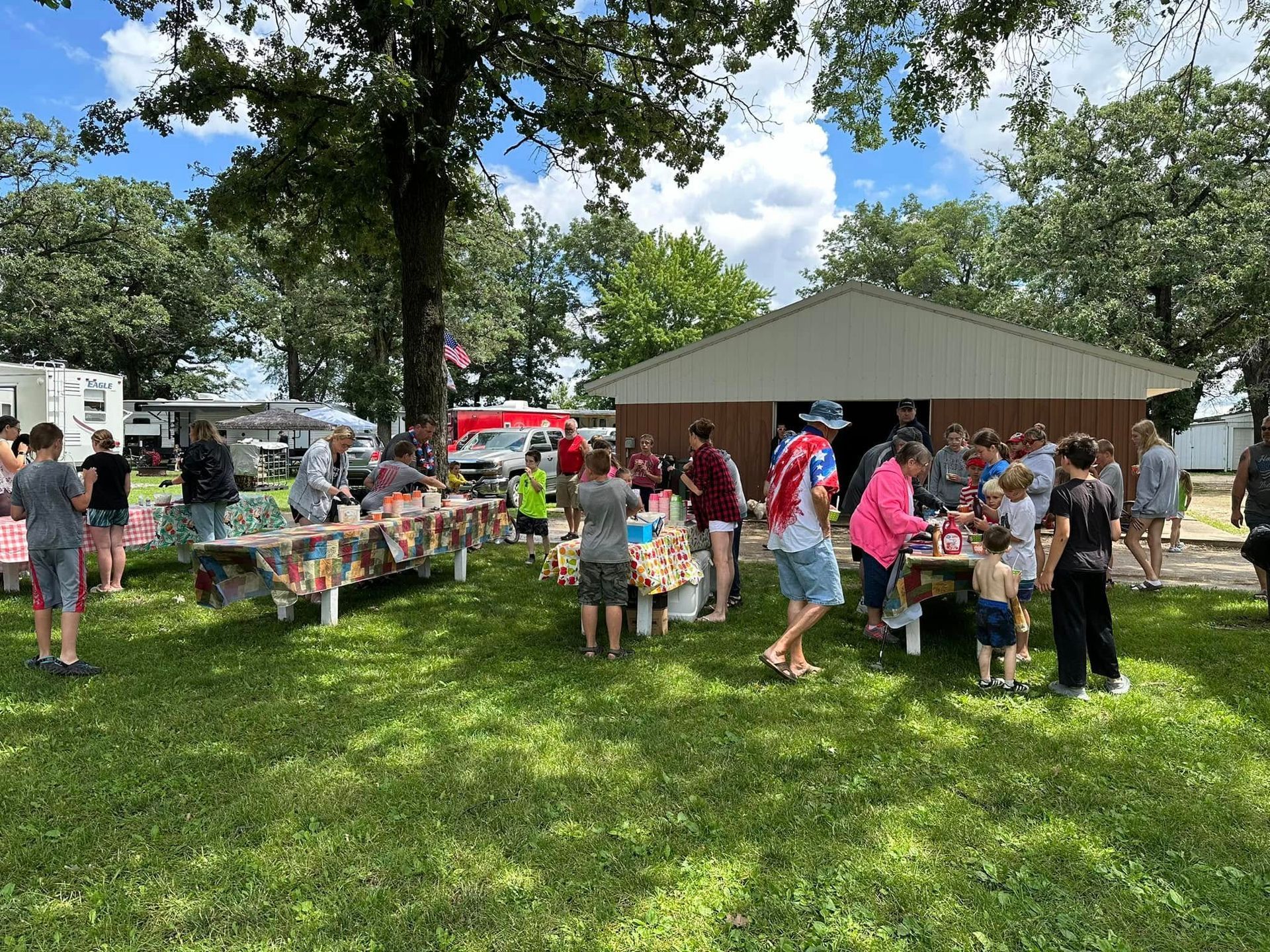 A group of people are standing around tables in a park.