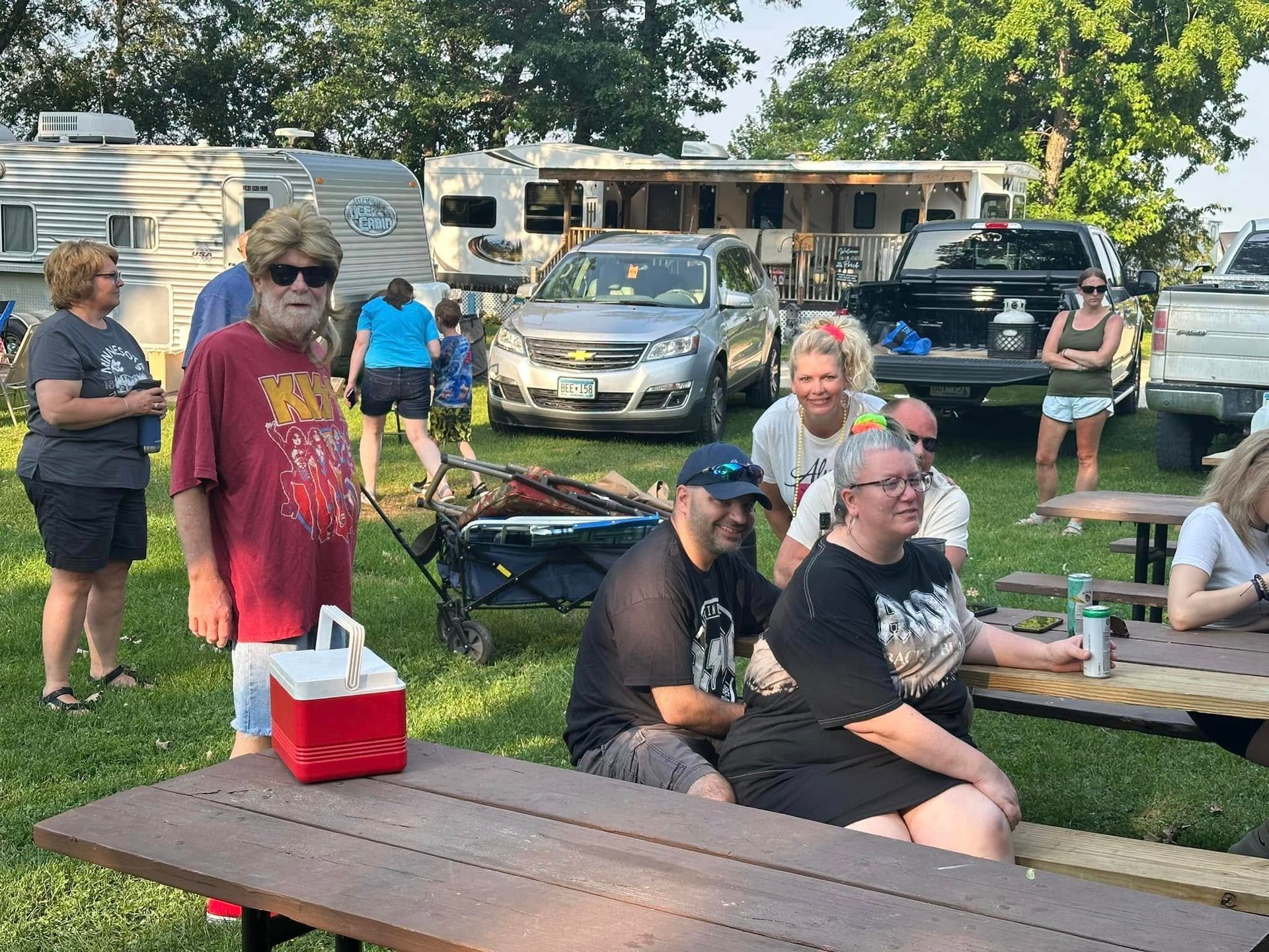 A group of people are sitting at picnic tables in a park.