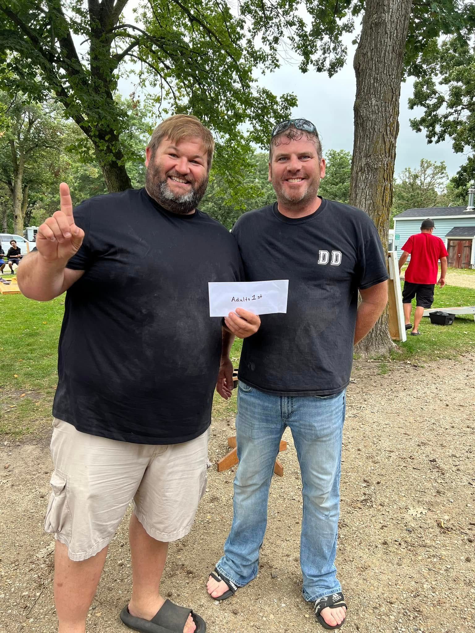 Two men are standing next to each other in a park holding a check.