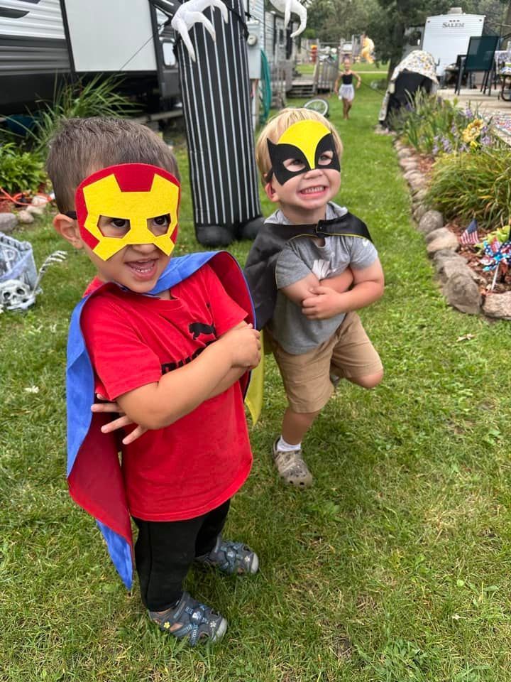 Two young boys wearing masks and capes are standing next to each other in the grass.