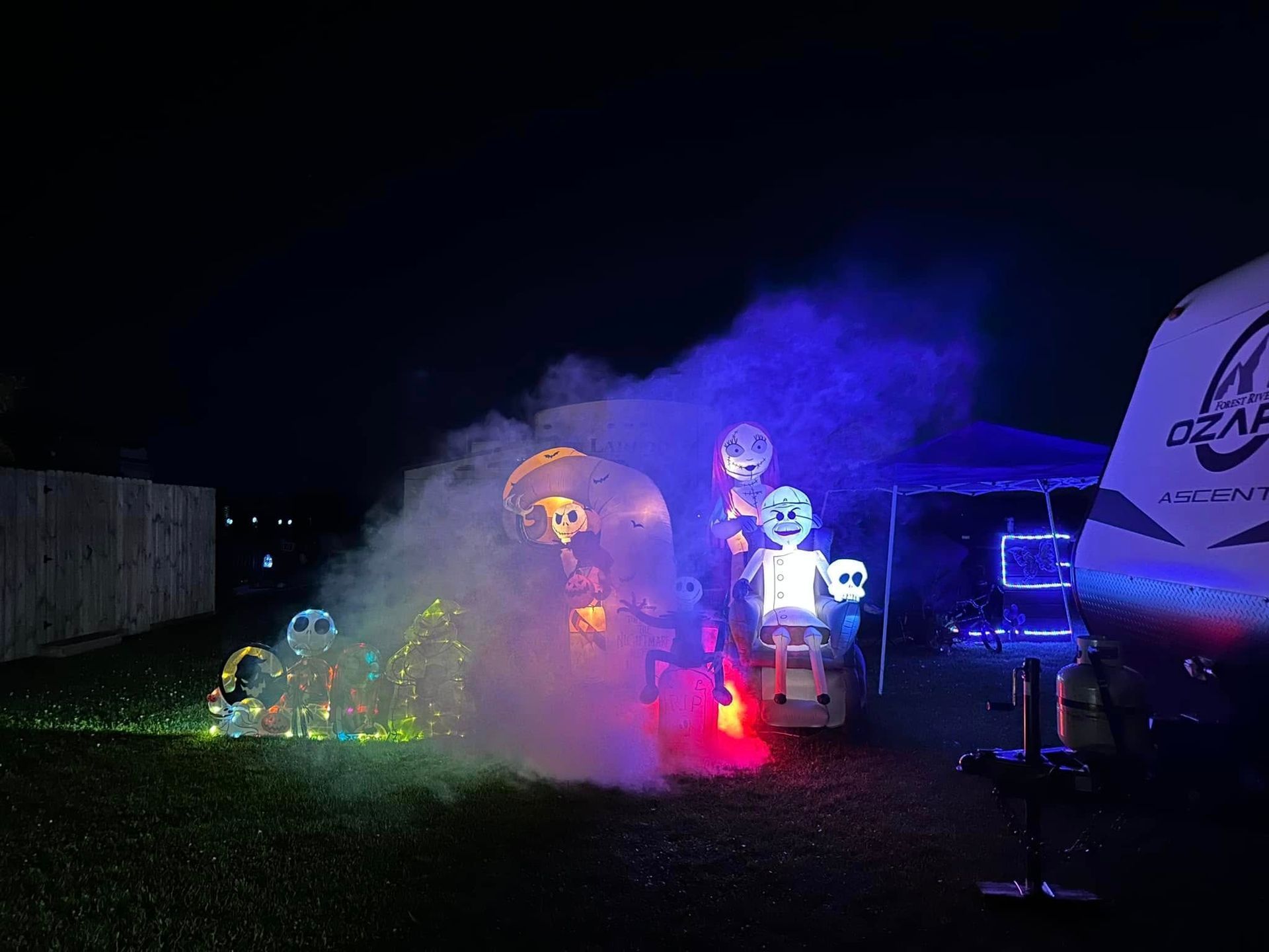 A group of skeletons are sitting in front of a trailer at night.