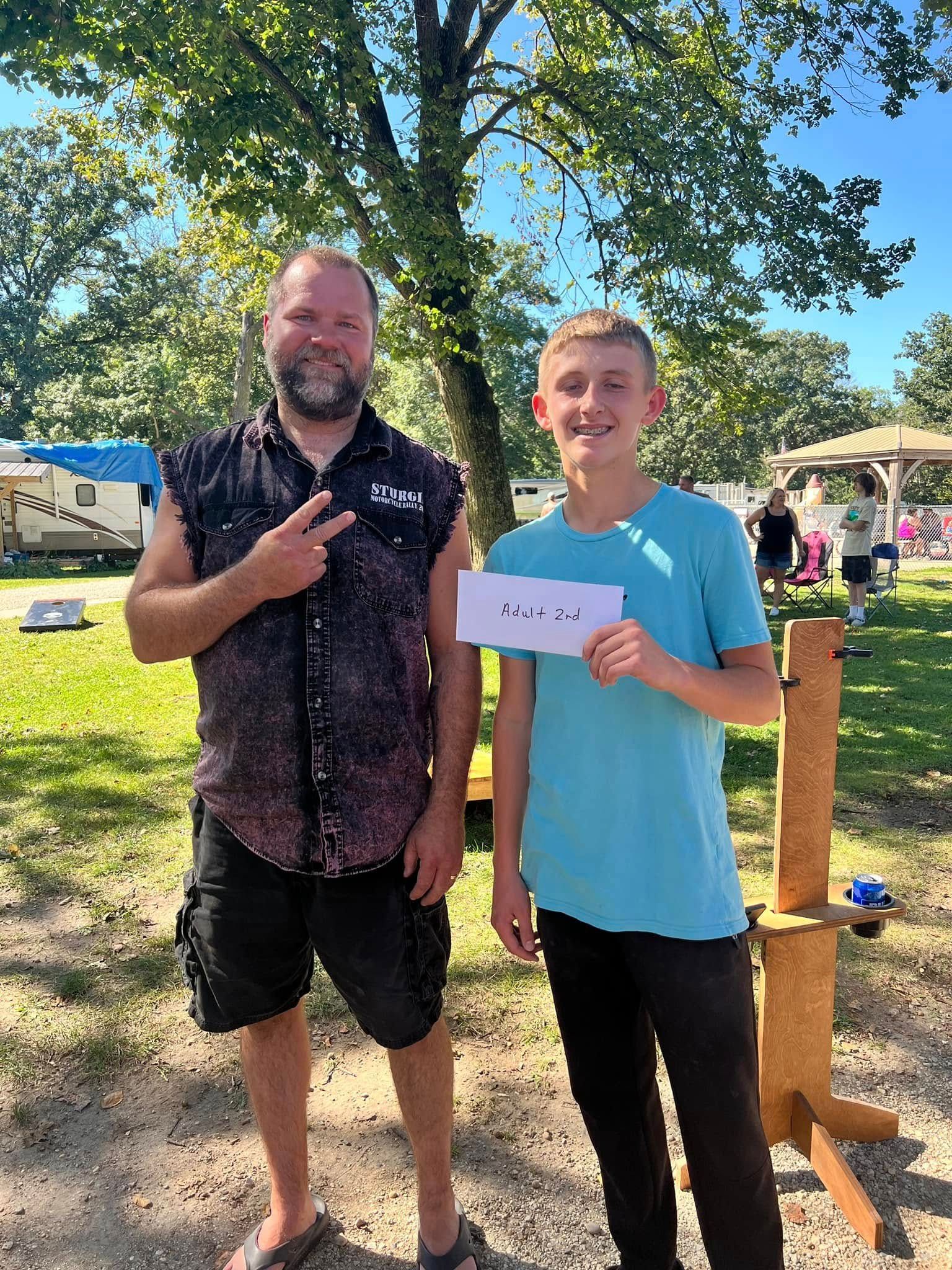 A man and a boy are standing next to each other in a park holding a paper.
