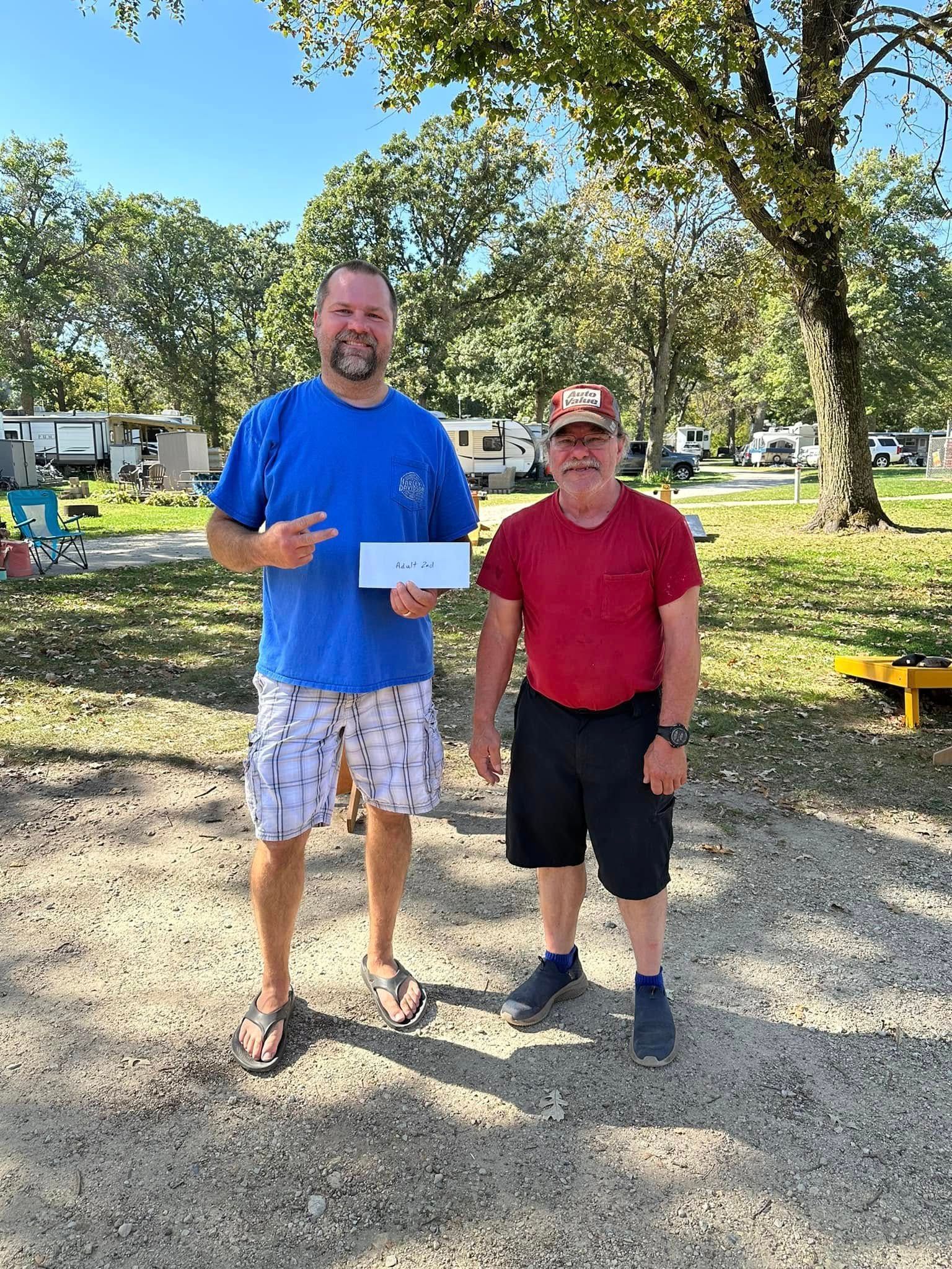 Two men are standing next to each other in a park holding a check.