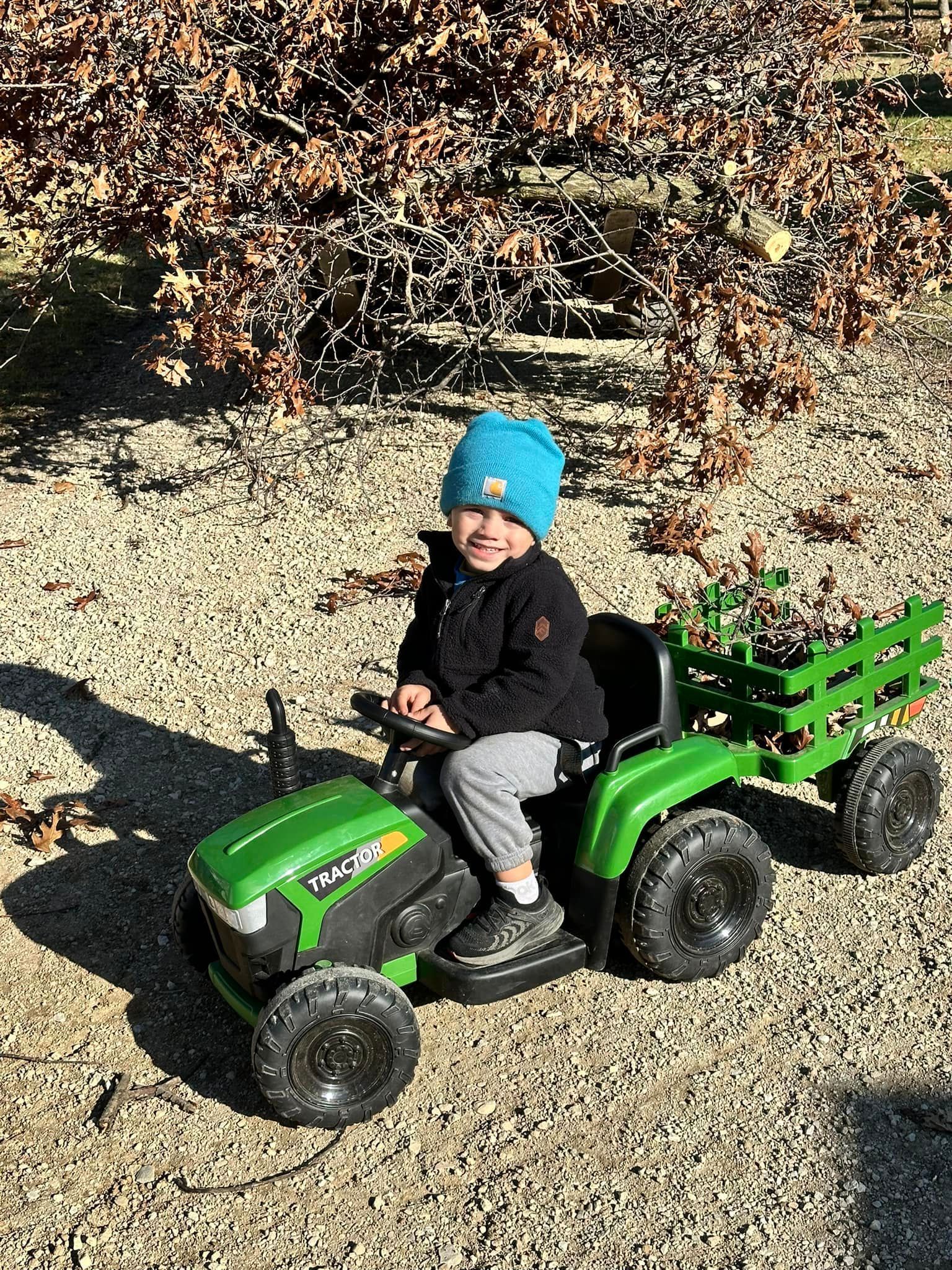 A little boy is sitting on a green toy tractor.