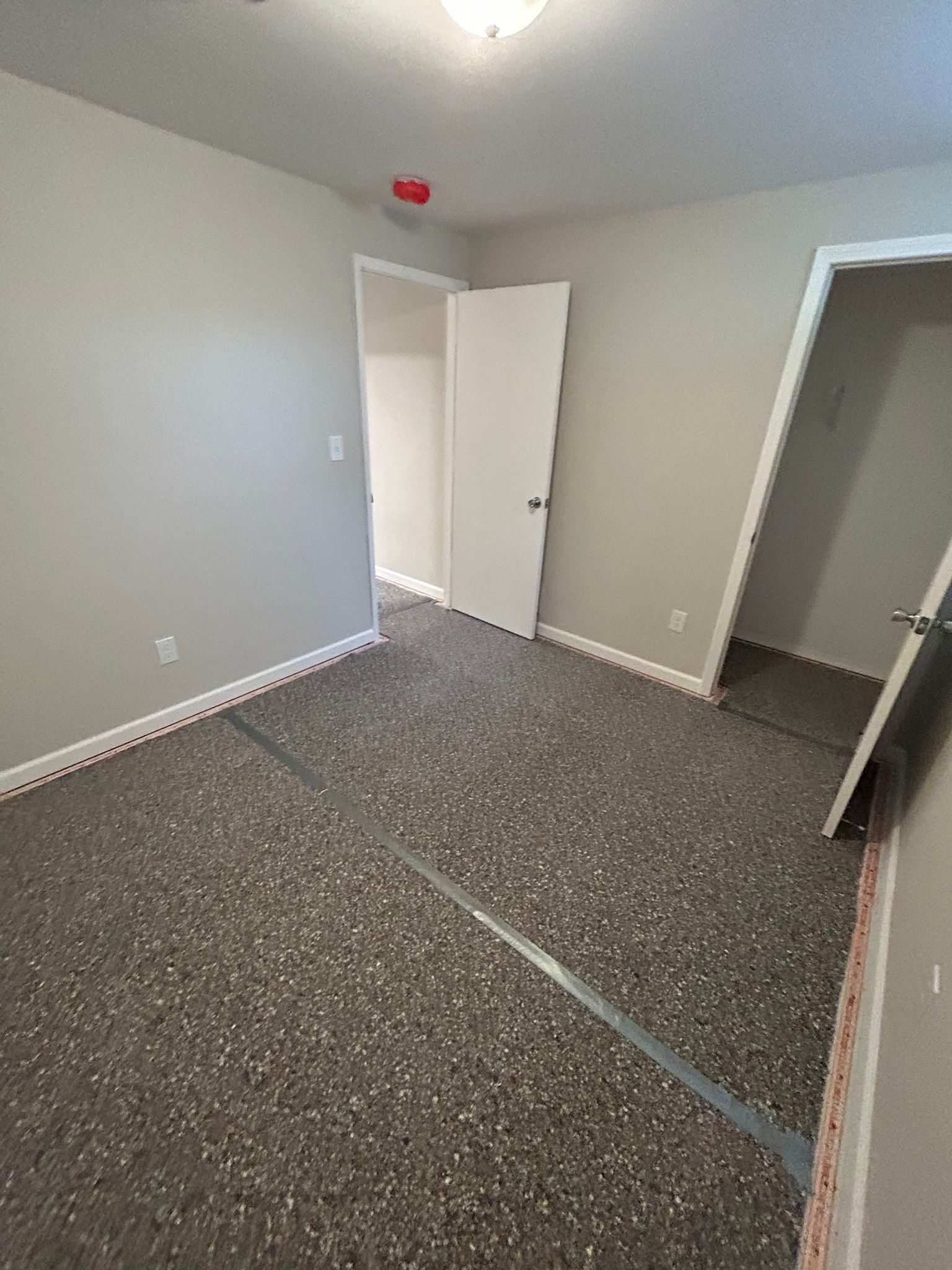 Empty room with gray walls and speckled flooring; two open doorways.