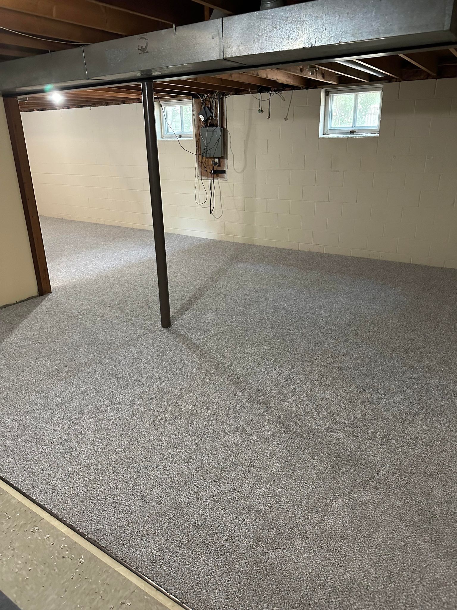 Basement with gray flecked flooring, concrete walls, and support beam. Two small windows visible.