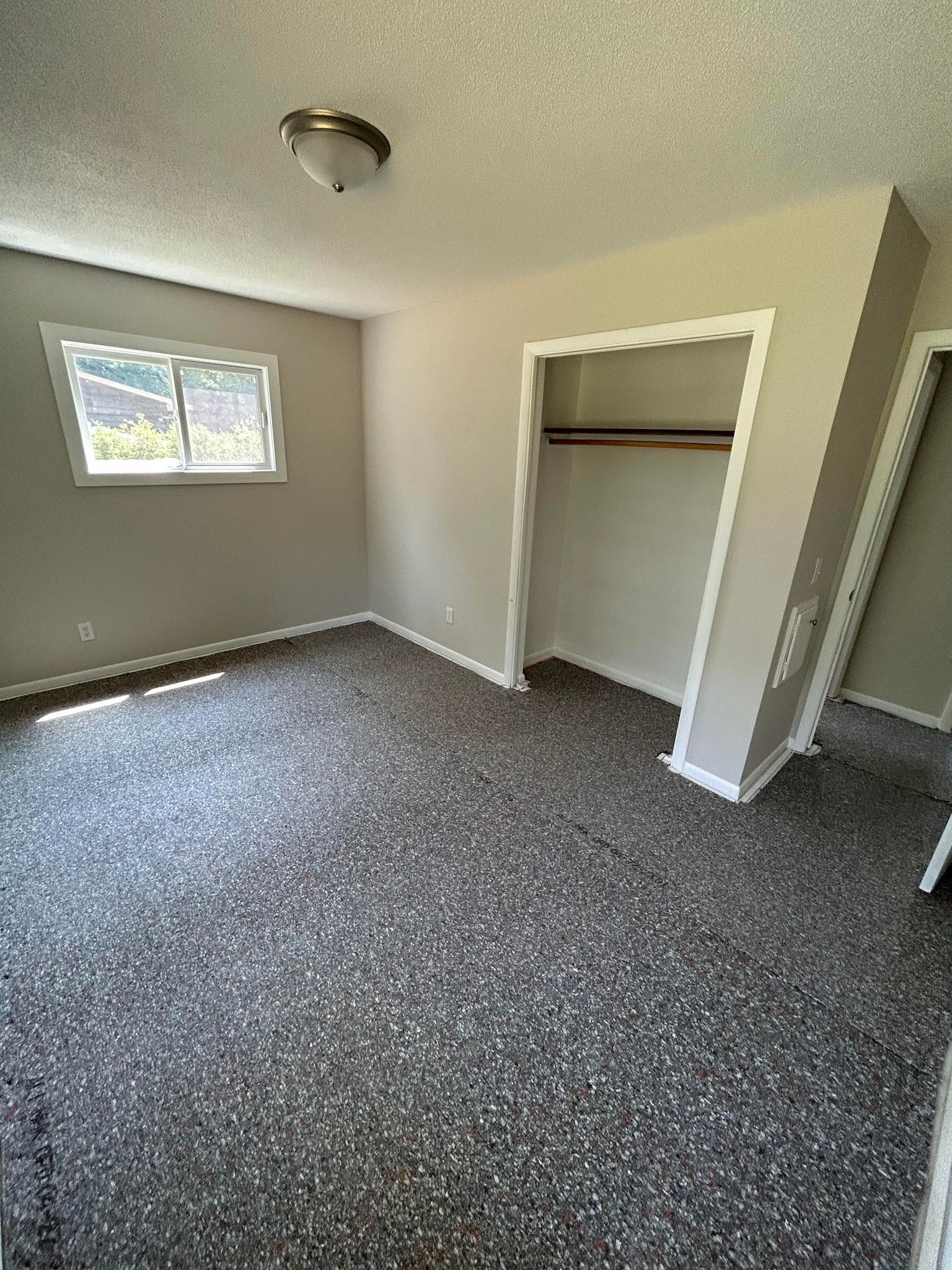 Empty room with grey carpet, beige walls, small window, and open closet.