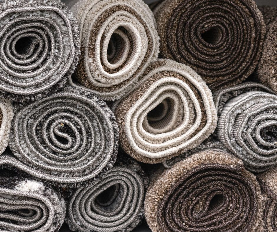 Rolled-up carpet samples in various shades of gray and brown, stacked together.