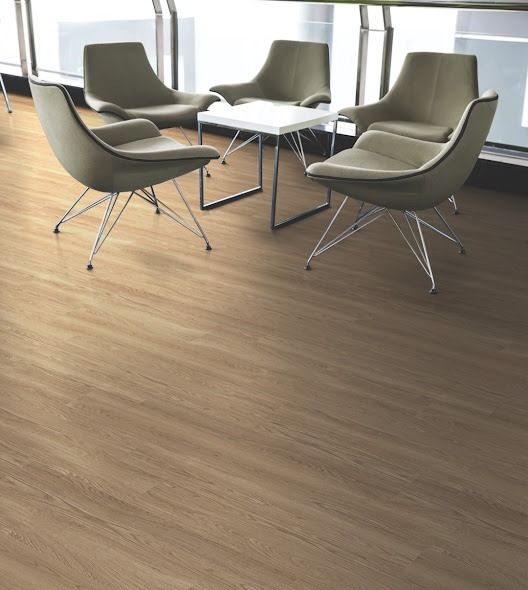 Four beige armchairs around a small white table on a wood-look floor, near a window.