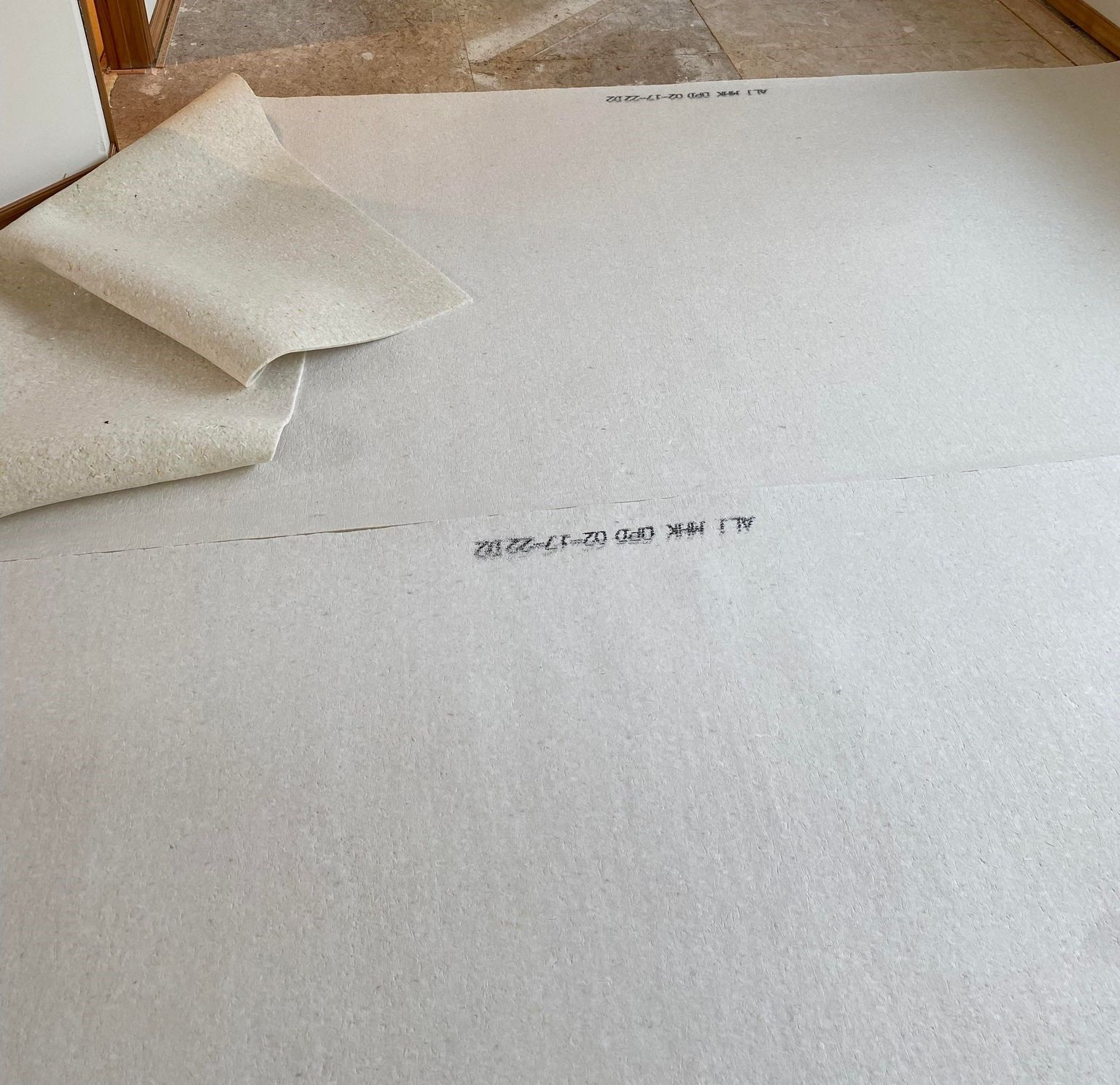 White floor underlayment laid on a subfloor, with a corner folded over.