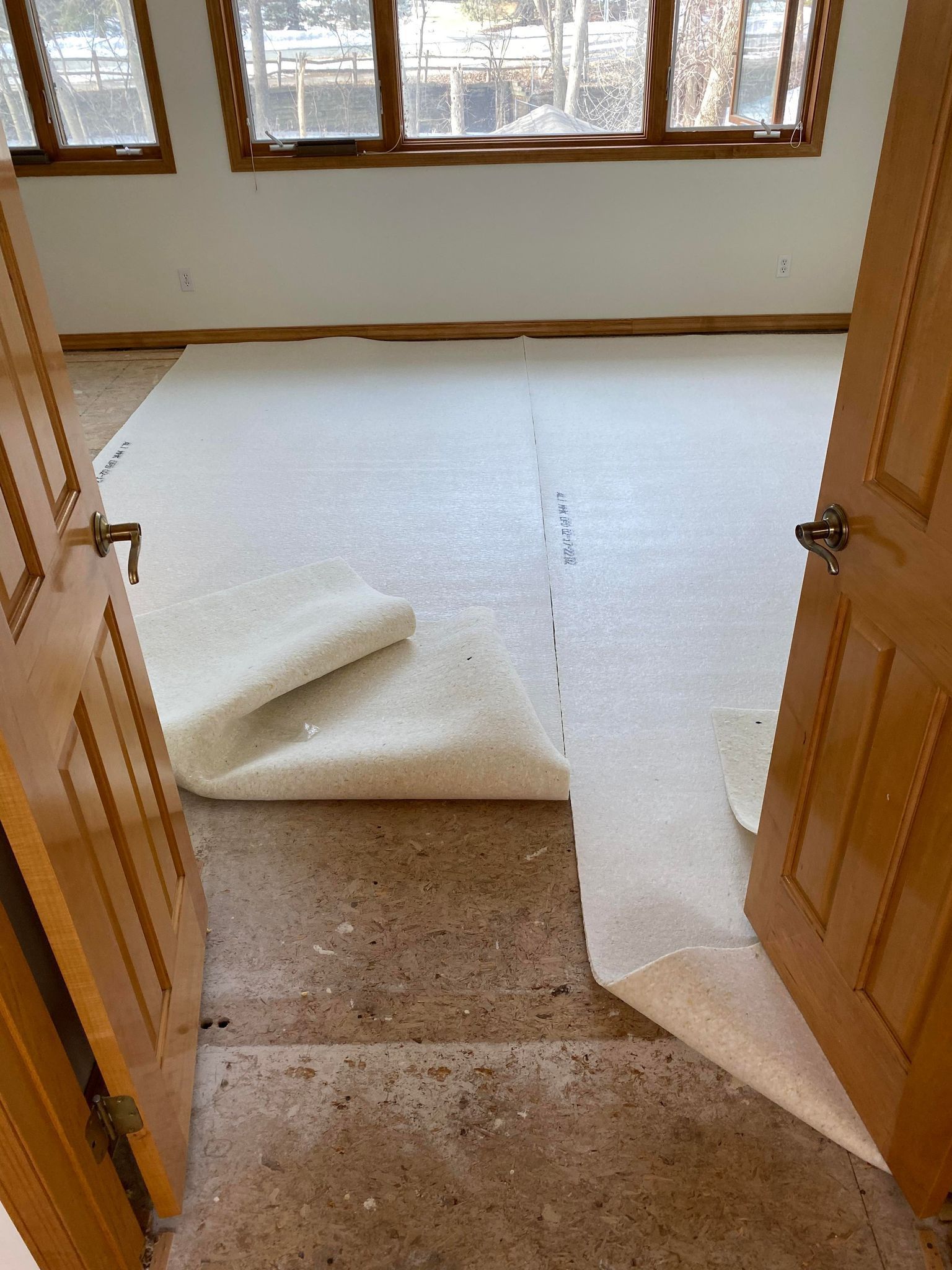 Interior view: carpet rolled out over speckled concrete floor in a room with wood doors and windows.